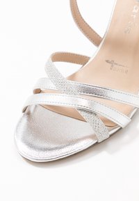 Srebrne metaliczne sandały na paskach o gładkiej fakturze i akcentach w brokacie. Miękka beżowa wkładka, minimalistyczny design, odkryty przód.