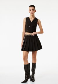 Brun randig kort väst med en ficka och knappar, parat med en veckad mini kjol och svarta knähöga stilettboots.