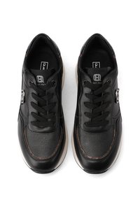 Un par de zapatillas de cuero negro con cordones negros, acentos de costura marrón y suelas blancas, vistas desde arriba sobre un fondo blanco.