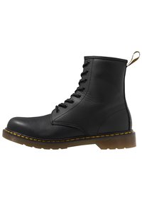 Bottine en cuir noir à lacets avec un bout arrondi, une semelle en caoutchouc et des accents de surpiqûres jaunes. Présente une languette au talon pour un enfilage facile.