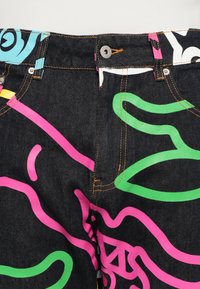 Black denim jeans featuring vibrant, abstract patterns in green, pink, and blue. Includes metal button and contrasting stitching details.