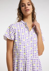 Rochie cu mânecă scurtă, dotată cu un rând de nasturi, din material alb cu un model de triunghiuri în nuanțe de violet și galben, și detaliu de talie strânsă.