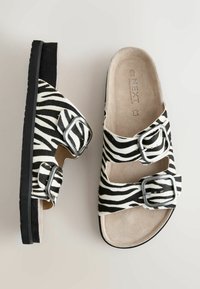 Sebratriibulised sandaalid, millel on kaks hõbedast pandlat, beežid tallad ja mustad pohjad, näidatud pealt- ja küljelt vaates.