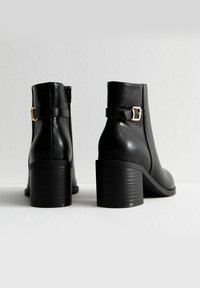 Botines de cuero negro con un acabado liso, que cuentan con una cremallera lateral, una hebilla decorativa y un tacón grueso y acanalado.