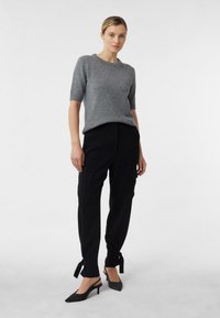 Szary sweter z krótkim rękawem i okrągłym dekoltem, zestawiony z czarnymi spodniami cargo z bocznymi kieszeniami i sznurkami przy nogawkach, uzupełniony czarnymi szpilkami.