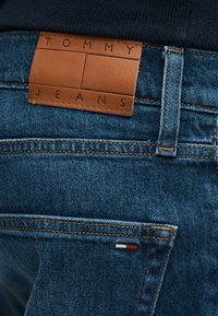 Sötétkék farmernadrág barna bőrből készült "Tommy Jeans" címkével és a hátsó zsebén kis, piros, fehér és kék hímzett logóval.