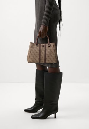 Femme en robe grise côtelée et bottes noires mi-mollet tenant un sac à main beige à motifs avec des poignées et des finitions marron.