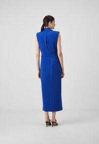 Oblé modré šaty bez rukávů s rozparkem na zadní straně a diskrétními kapsami; hladká tkanina s elegantním, prodlouženým siluetou.