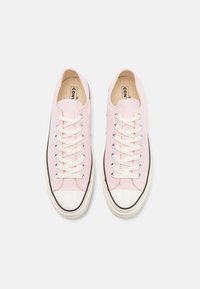 Sneakers in tela rosa chiaro con punta in gomma bianca, linea di accento nera e lacci bianchi. Parte superiore testurizzata e suola piatta.