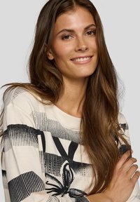 Langärmliges Creme-Shirt mit schwarzem Streifenmuster, floralem grafischen Detail und rundem Ausschnitt, gefertigt aus weichem Baumwollmaterial.