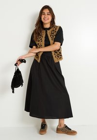 Chaleco de pelaje con estampado de leopardo sobre una camiseta negra, combinado con una falda negra vaporosa y zapatos con estampado de leopardo, sosteniendo un pequeño bolso negro.