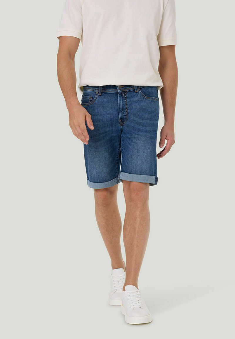 Herren-Denim-Shorts in einem mittleren Blauton, mit einem Fünf-Taschen-Design, umgeschlagenen Säumen und einem Reißverschluss, kombiniert mit weißen Sneakers.