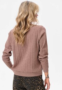 Bruin geribd trui met lange mouwen en een ronde hals, voorzien van een gestructureerde stof. Gecombineerd met een broek in luipaardprint.