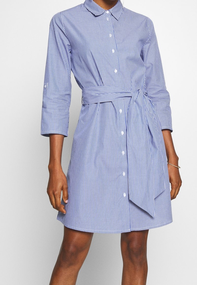 Robe chemise rayée en bleu et blanc, dotée d'un col, de manches longues, de boutons sur le devant et d'une ceinture nouée à la taille pour un ajustement réglable.
