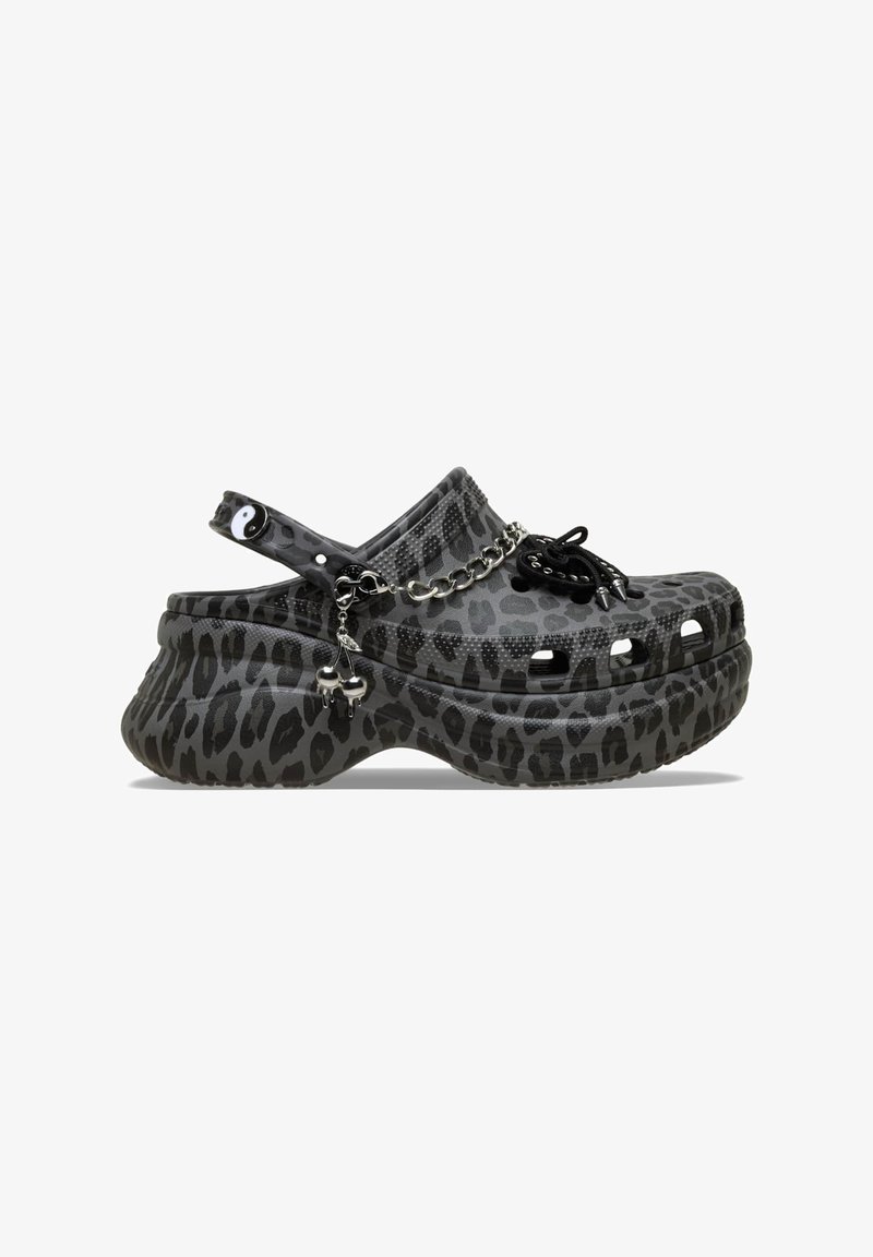 Schwarze Clogs mit Leopardenmuster und robuster Sohle, mit einer Kettenapplikation, Schnürdetails und dekorativen Charms an der Seite.