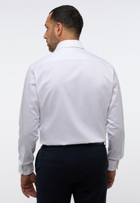 Witte lange mouwen overhemd met een klassiek kraag en knoopmanchetten, gecombineerd met donkere broeken, gezien vanuit de achterkant. Gladde textuur, op maat gemaakte pasvorm.