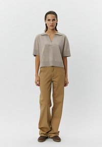 Béžový pletený top v polo štýle s výstrihom do V a krátkymi rukávmi, skombinovaný s svetlohnedými širokými nohavicami a hnedými topánkami.