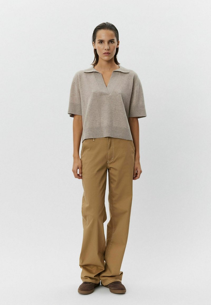 Béžový pletený top v polo štýle s výstrihom do V a krátkymi rukávmi, skombinovaný s svetlohnedými širokými nohavicami a hnedými topánkami.