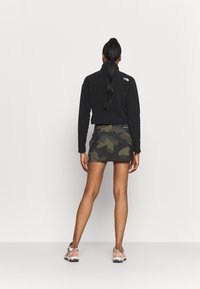 Sudadera negra de forro polar con cuello alto, combinada con una falda de estampado camuflaje. El calzado presenta un diseño de malla texturizada en tonos rosas y grises.