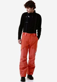 Pantaloni da sci impermeabili arancioni con bretelle nere regolabili, ginocchia rinforzate e logo Kappa visibile sulla gamba. Finitura in tessuto texture.