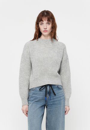 Pull en tricot gris avec une finition texturée, encolure ronde et poignets côtelés. Porté avec un jean en denim bleu taille haute avec un cordon de serrage noir.