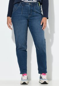 Jeans de talle alto de color azul oscuro con piernas rectas, que presentan bolsillos frontales y costuras en contraste, combinados con zapatillas de color claro.