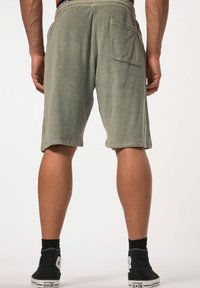 Shorts de rizo gris con cintura elástica, que cuentan con un único bolsillo trasero y un corte relajado, llevados con zapatillas negras tipo high-top.