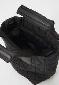Czarna pikowana torebka na ramię o miękkiej, wyściełanej fakturze, z dwiema rączkami i wewnętrzną kieszenią na zamek. Wnętrze to beżowy materiał.