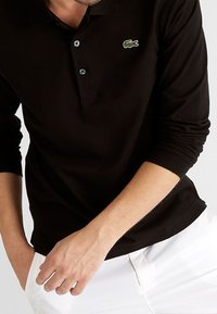 Svart långärmad polo tröja i bomull, med en tre-knappsknäppning och en grön krokodil-logga på vänster bröst.