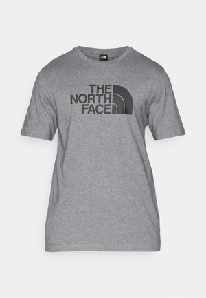 Camiseta de manga corta gris hecha de una mezcla de algodón, con un estampado gráfico negro de "THE NORTH FACE" y un detalle de logo curvado en la parte frontal.