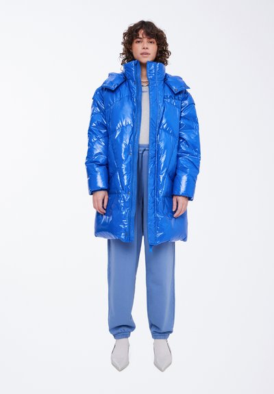 Mėlynas pūkinis paltas su aukštu apykakle, blizgia textura ir per dideliu fasonu. Užtrauktuko uždarymas ir dvi šoninės kišenės. Derinamas su šviesiai mėlynomis kelnėmis.