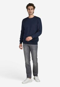 Marineblauwe crewneck sweatshirt met lange mouwen, van een katoenmix. Gecombineerd met grijze spijkerbroeken en witte sneakers, staande op een witte achtergrond.