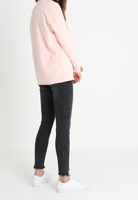 Svetle růžová mikina s dlouhým rukávem v kombinaci s černými skinny džíny. Džíny mají třepané lemy; bílými teniskami je outfit doplněn.