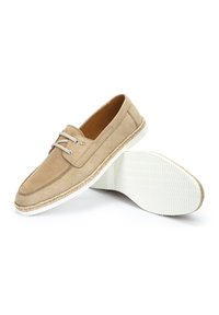 Zapatos de ante beige con un perfil bajo, suelas de goma blanca y cordones decorativos. Presentan acentos cosidos y un acabado texturizado.