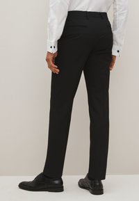 Zwarte op maat gemaakte broeken met een rechte pasvorm, platte voorkant en zijzakken. Gecombineerd met zwarte dress schoenen en een wit shirt met manchetknopen.