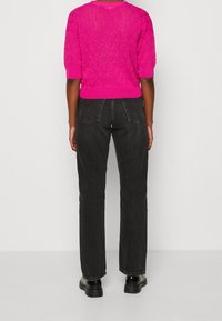 Suéter de punto fucsia con mangas cortas, que presenta un patrón de diamantes; combinado con jeans negros de pierna recta y zapatos negros con cordones.