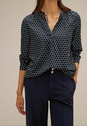 Mörkblå blus med vita prickar, lättviktigt tyg, v-ringning, knapprad, lång ärm, samt kombinerad med mörkblå byxor.