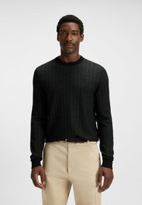 Svart tröja med herringbone-mönster, rund hals och ribbade mudd. Matchad med beige byxor och ett svart bälte.
