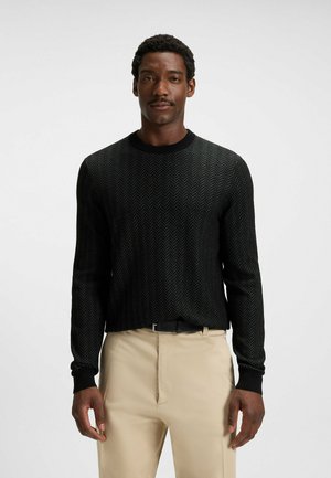 Svart tröja med herringbone-mönster, rund hals och ribbade mudd. Matchad med beige byxor och ett svart bälte.