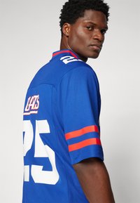 Maillot bleu avec le numéro blanc "25" et le texte "CATS". Accents rayés rouges et bleus sur les manches. Fabriqué en tissu texturé.
