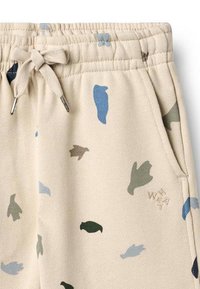 Pantalones deportivos beige con siluetas de animales en varios colores, azul, verde y negro. Cuentan con una cintura elástica y detalle de cordón ajustable.