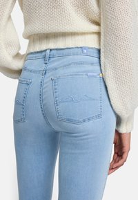 Jasnoniebieskie dżinsy z wysokim stanem, pięcioma kieszeniami i haftowanymi tylnymi kieszeniami. Tkanina ma gładką strukturę i lekki strecz.