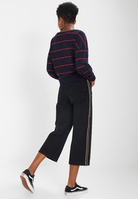 Sudadera de rayas marinas con líneas rojas, combinada con jeans de pierna ancha negros que presentan un detalle de raya lateral. Unas zapatillas Vans negras completan el conjunto.