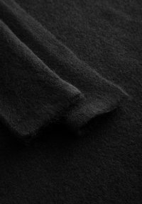 Czarna wełniana tkanina o miękkiej, teksturowanej powierzchni; dwa nakładające się kawałki pokazujące subtelny połysk i lekkie strzępienie na krawędziach.