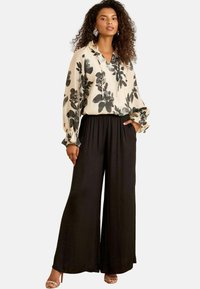 Floral blouse in cream with black and teal flowers, paired with wide-leg black pants. Features a relaxed fit and elastic waistband.