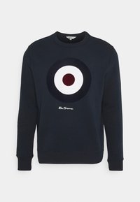 Granatowa bluza z dużym okrągłym nadrukiem w kolorach białym, ciemnoniebieskim i bordowym. Posiada okrągły dekolt i ściągacze na rękawach, z markowym logo „Ben Sherman”.