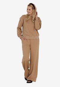 Beżowy sweatshirt z okrągłym dekoltem i ribbentem na dole, w zestawieniu z pasującymi szerokimi spodniami. Gładki, miękki materiał o luźnym kroju.
