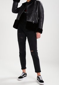 Svart läderjacka med fuskpälsärmar, kombinerad med svarta trasiga jeans och svarta Vans-sneakers. Minimalistisk design med metallisk dragkedjedetaljer.