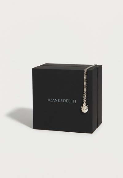 Μαύρο κουτί Alan Crocetti με ασημί κρεμαστό κόσμημα σε σχήμα φλόγας κρεμασμένο στη γωνία σε απλό λευκό φόντο.