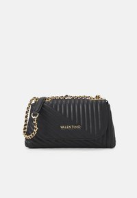 Svart, vadderad läderhandväska med ett diagonalt mönster, guld-tonad kedjestrappp, och en varumärkeslogotyp på den främre panelen.